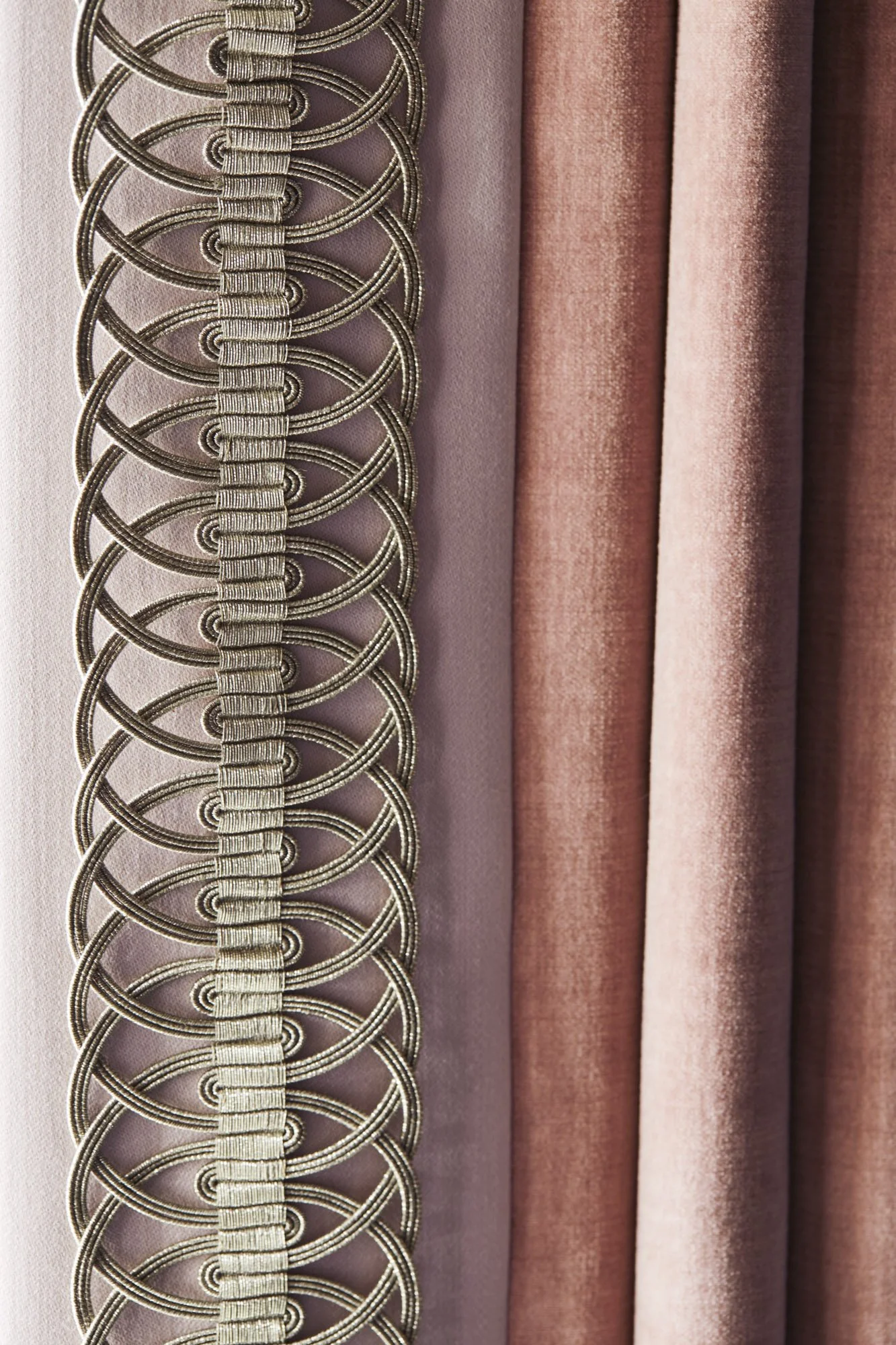 Close-up of softly textured pink and beige curtain fabric finished with intricate decorative braid trim.