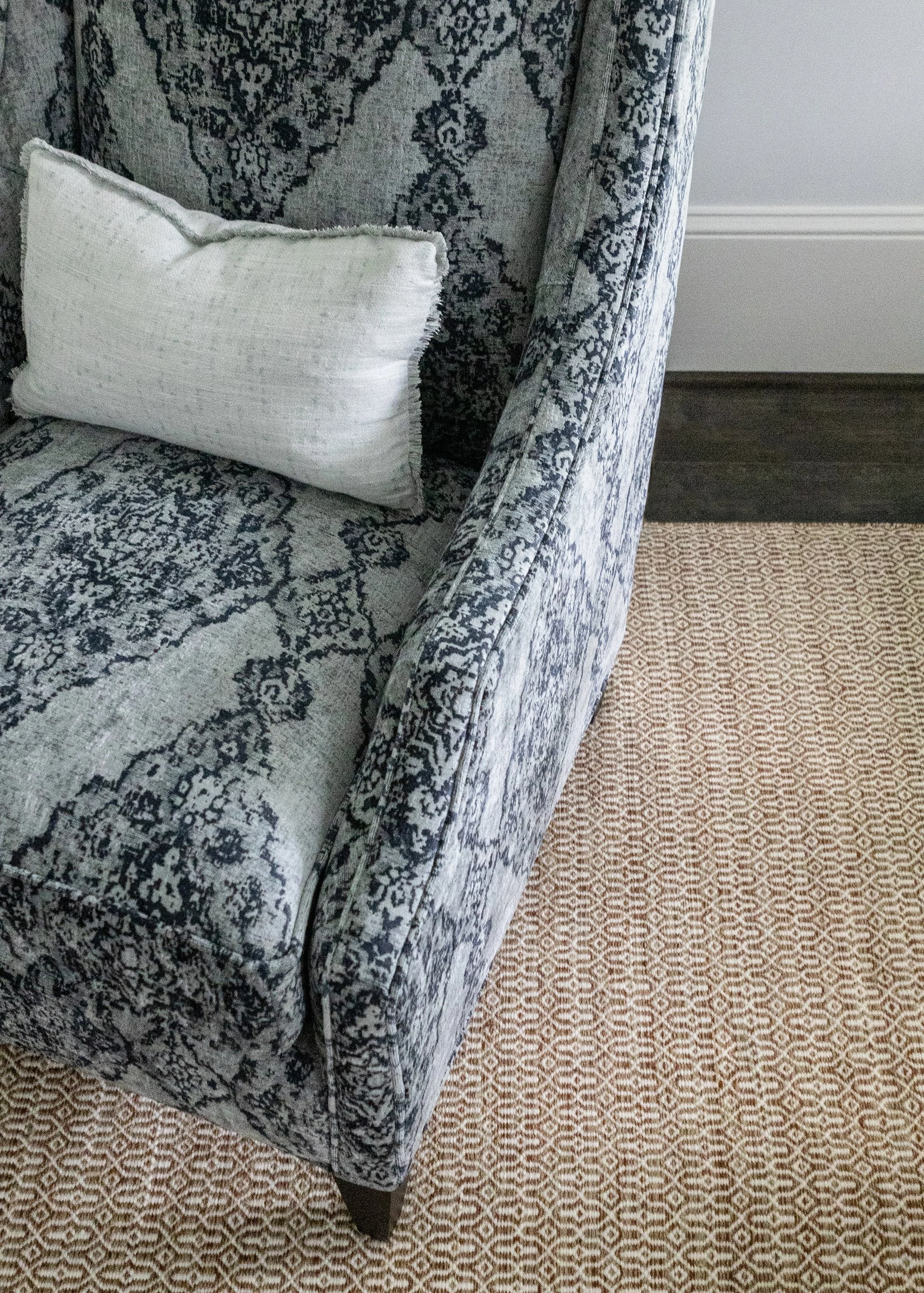 Patterned armchair with a white accent pillow positioned on a textured area rug.