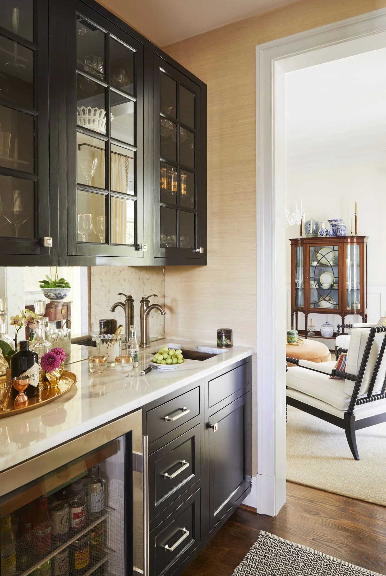 Kitchen bar area with dark cabinetry, glassware, a marble countertop, brass faucet, and a drinks tray with grapes.