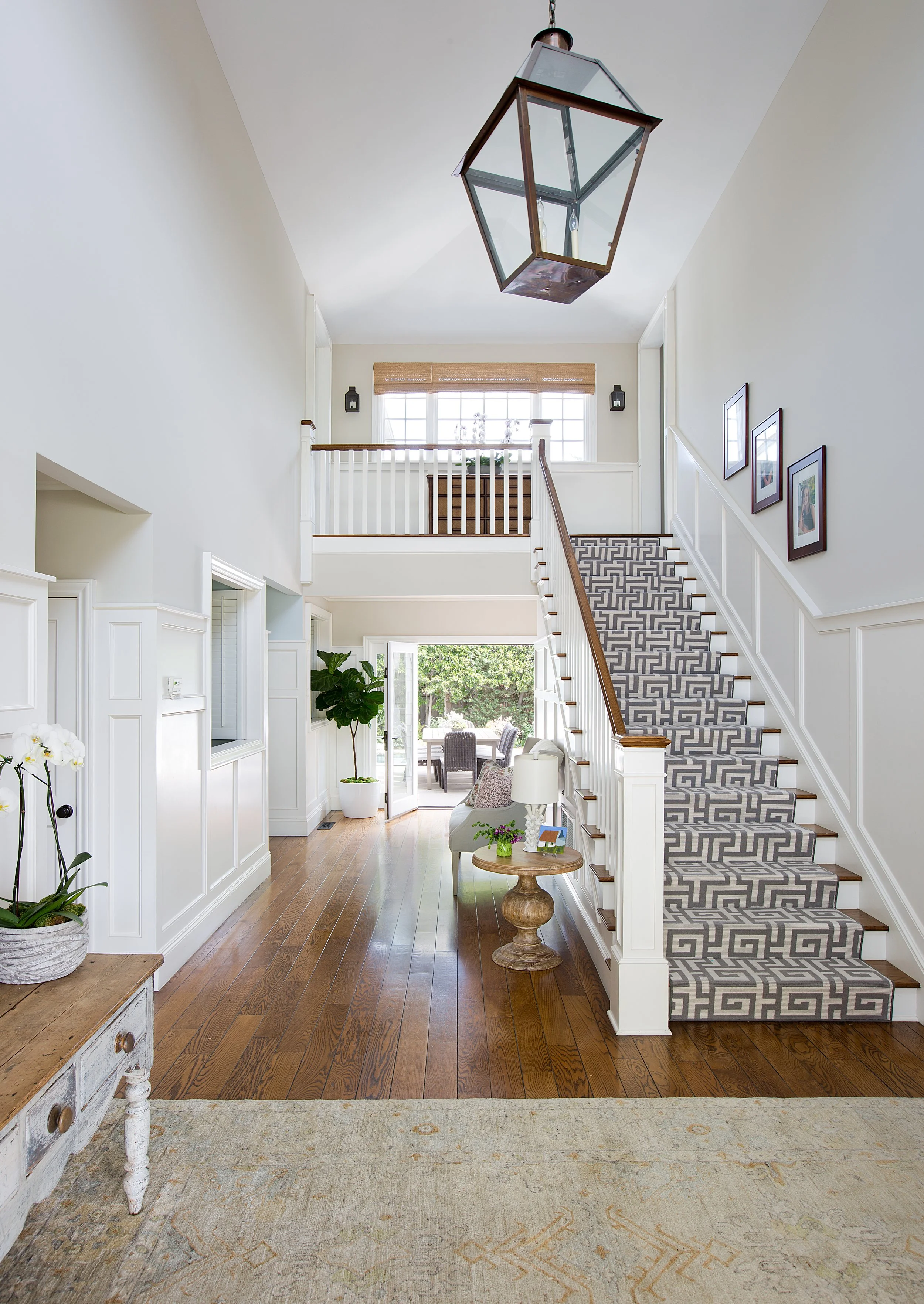 Open Pacific Palisades foyer with wood flooring, a patterned staircase runner, large chandelier, potted plants, and glass doors to the patio.