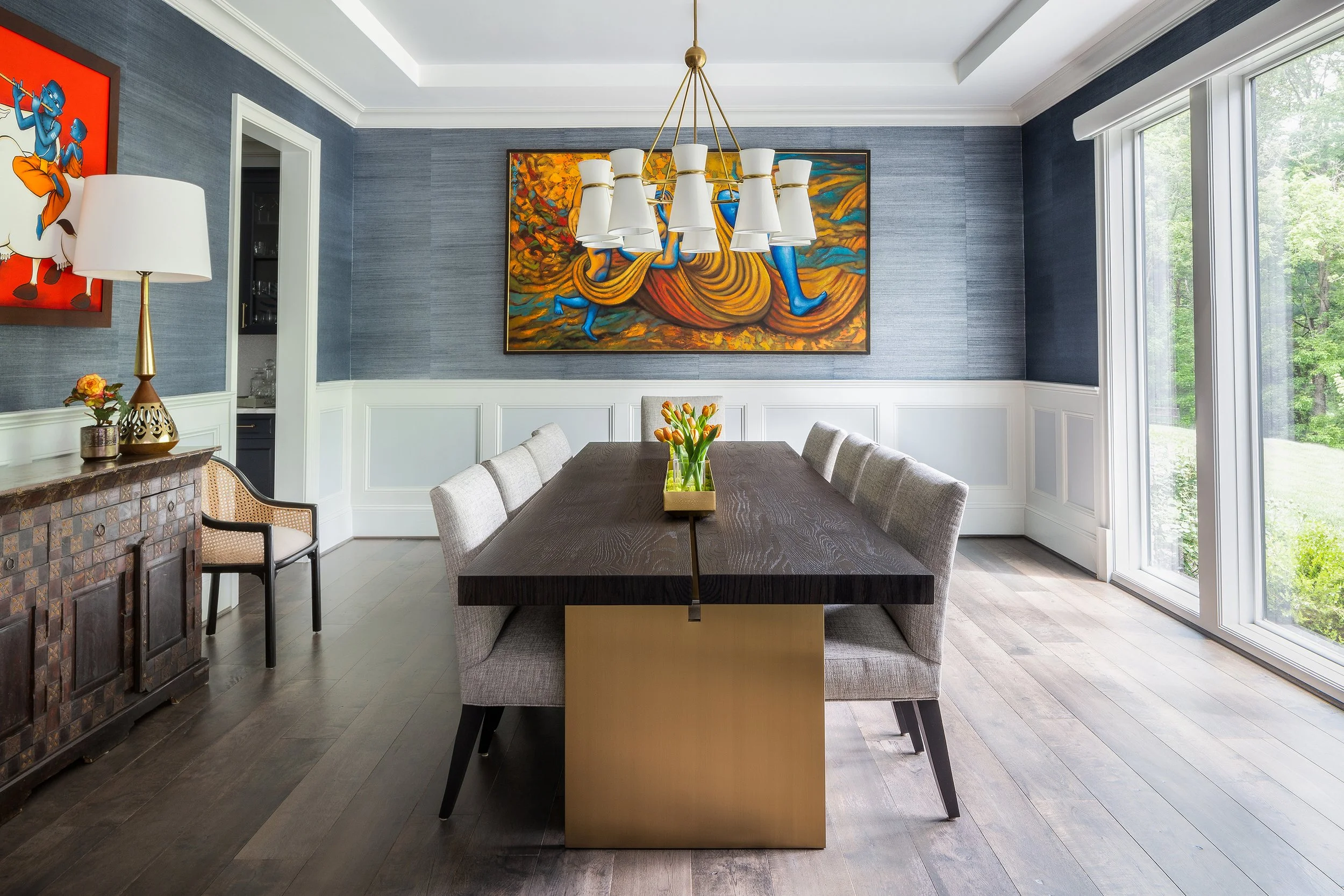 Dining room with a dark wood table, upholstered chairs, chandelier, colorful abstract artwork, sideboard, and large windows.