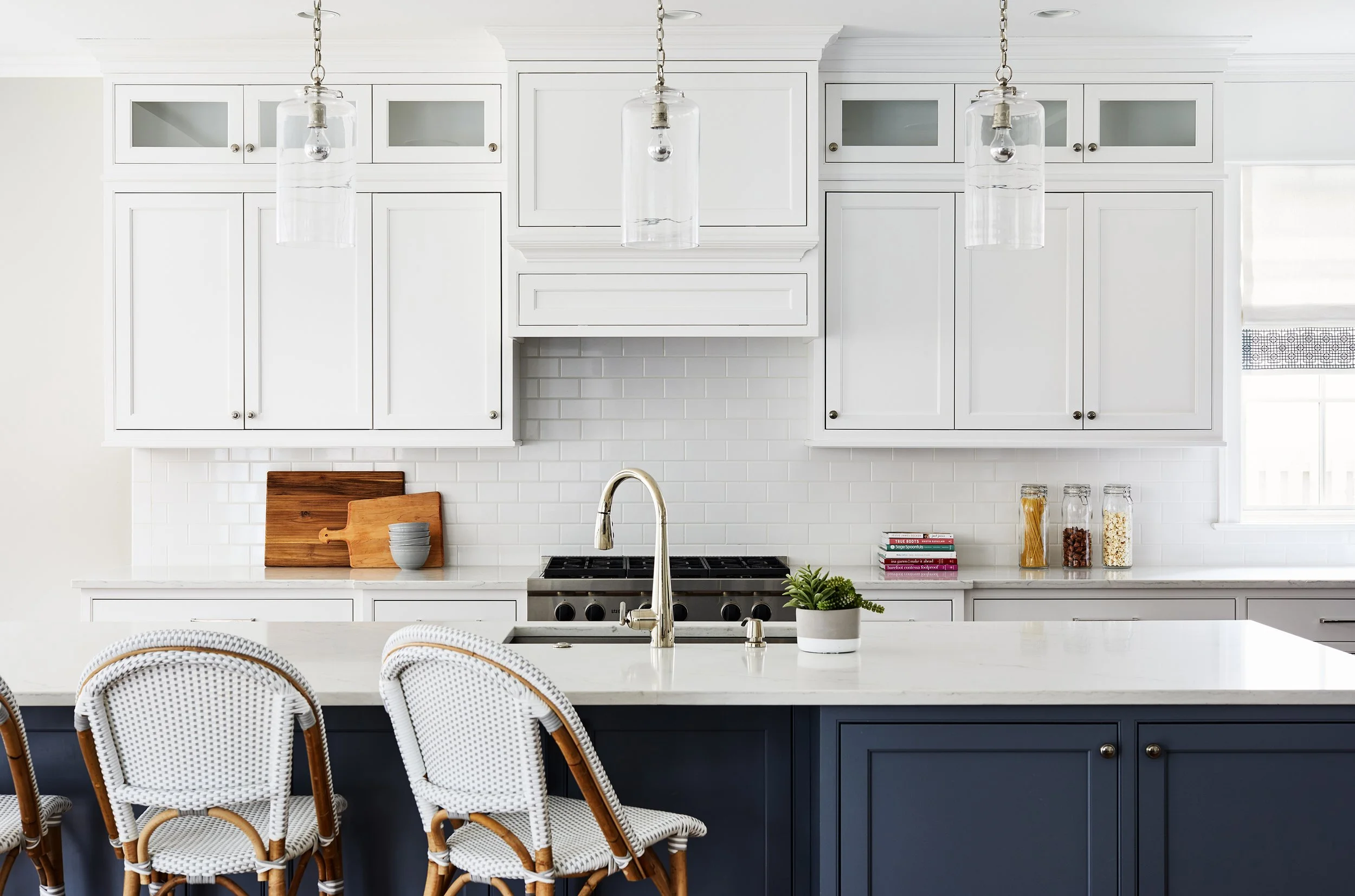 Family kitchen with white cabinetry, a large island, woven counter stools, pendant lights, stainless steel faucet, and styled countertops.