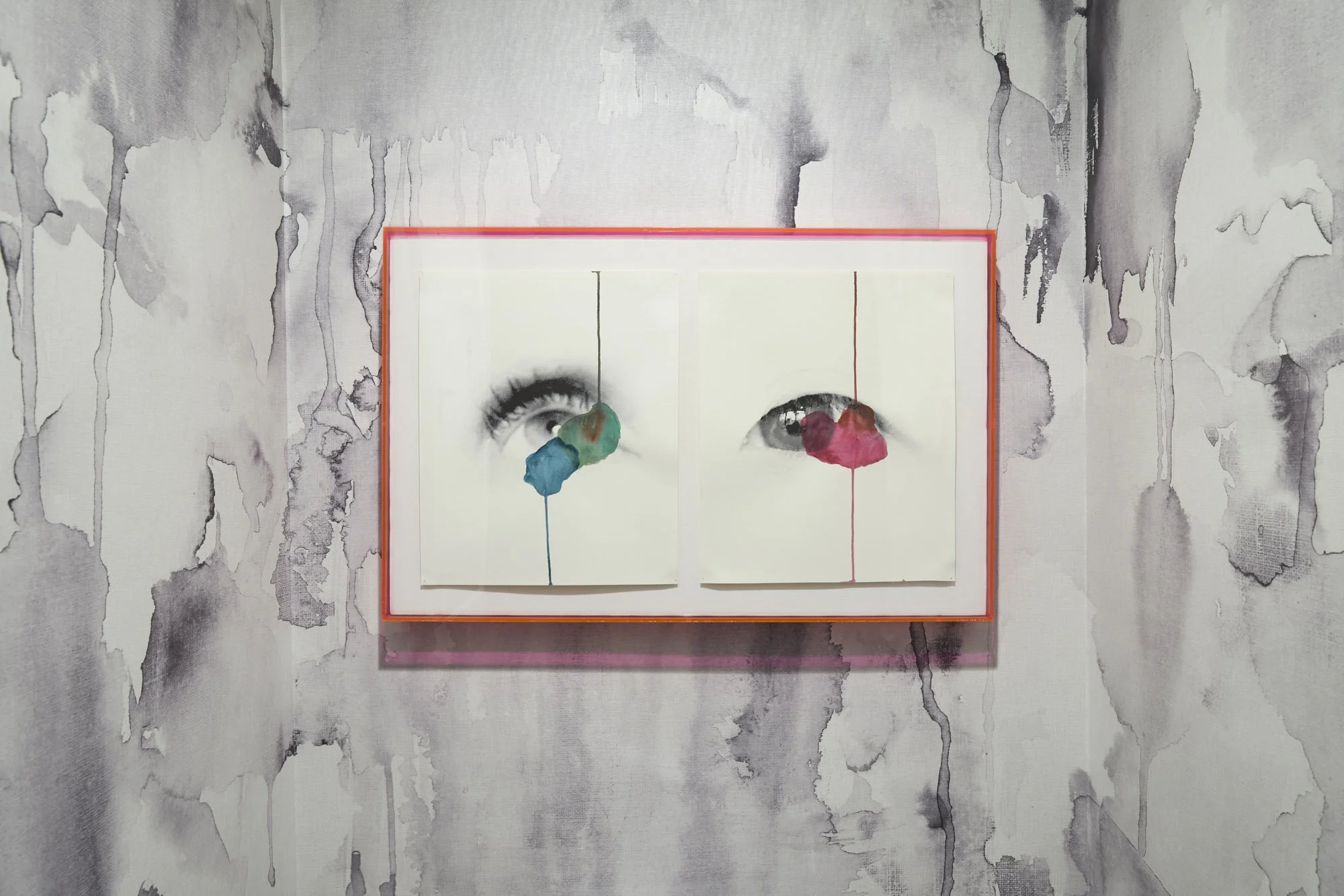 Two framed black-and-white eye illustrations with colorful watercolor accents displayed against a textured wall.