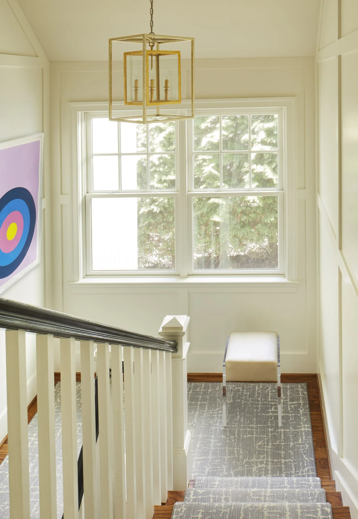 Staircase with white railings, a patterned runner, geometric pendant light, abstract artwork, and a small bench.
