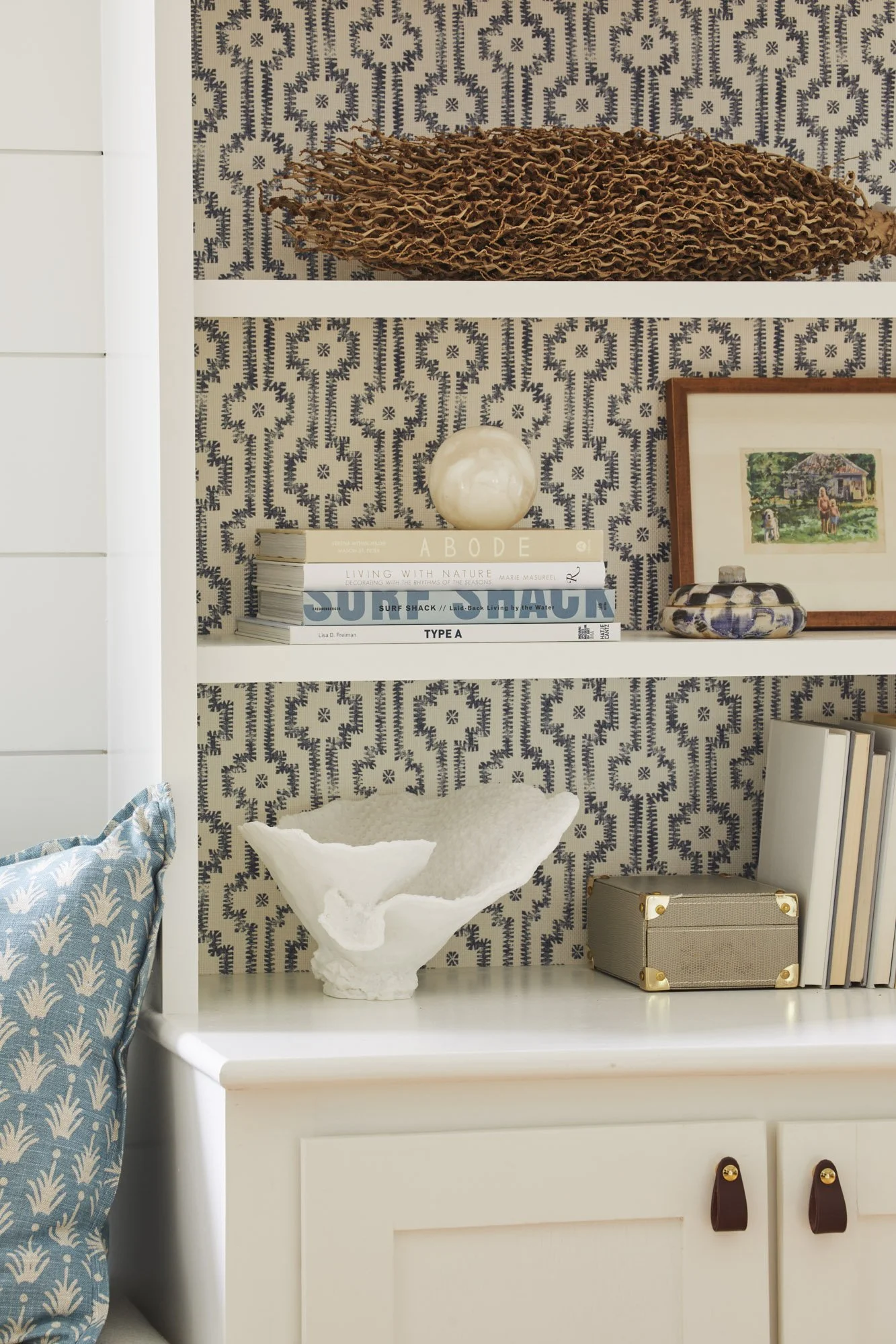 Built-in bookshelf styled with books, framed art, and collected objects against patterned wallpaper.