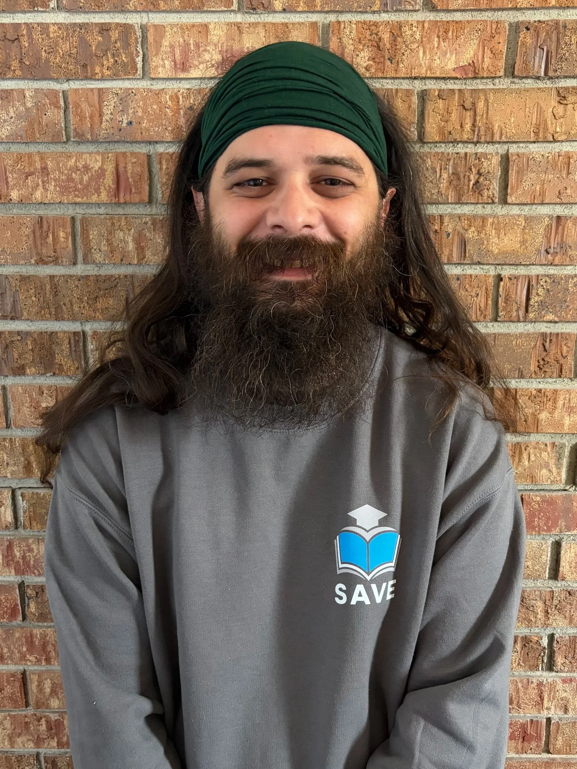A man with long hair, a beard, and a colorful headscarf smiling, wearing a blue sweatshirt that says 'Play Local' with a graphic of the state of Oregon.