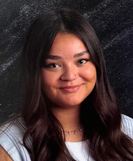 A young woman with long dark hair smiling, wearing a light-colored top and a necklace, against a dark, textured background.