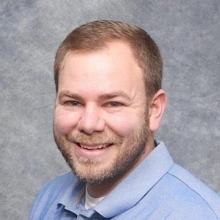 Man with short brown hair and a beard smiling in a blue shirt