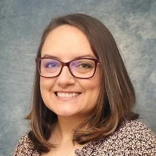 Portrait of a smiling woman with glasses and shoulder-length brown hair.
