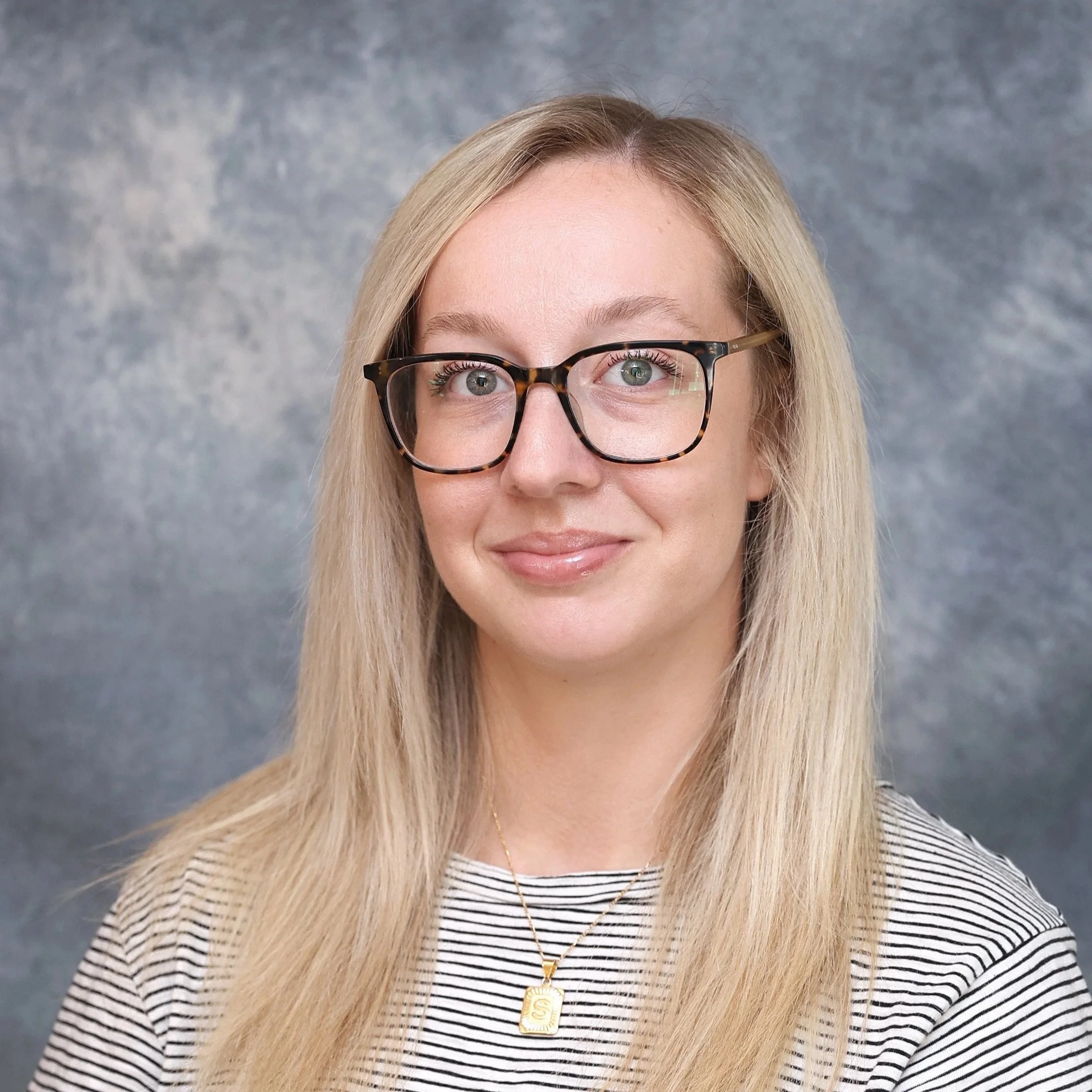 Portrait of a woman with blonde hair wearing glasses and a striped shirt.