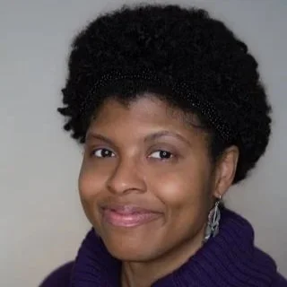 Portrait of a woman with short black hair wearing a purple sweater and silver earrings.