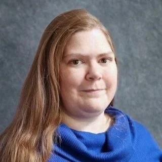 Portrait of a woman with long reddish-blonde hair wearing a blue turtleneck sweater.
