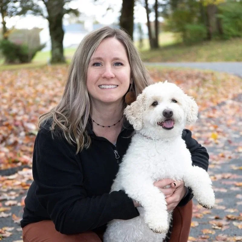 Woman crouching with a happy white small dog in an autumn park setting.