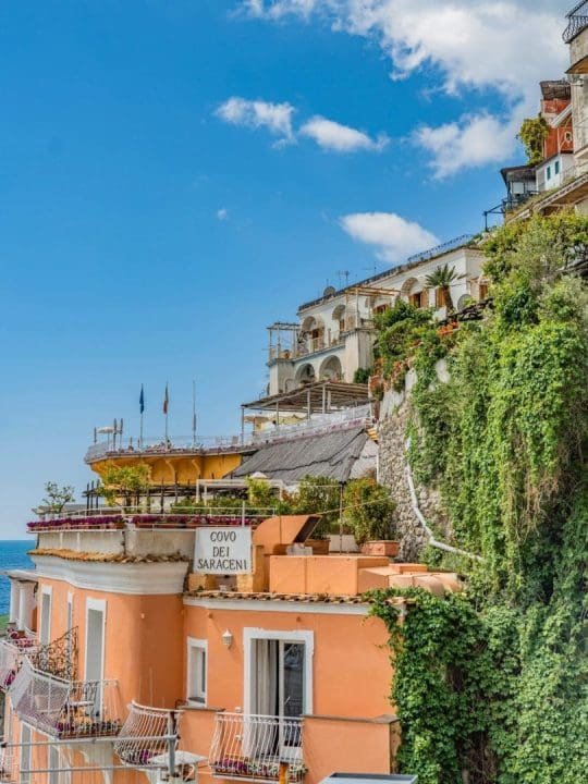 Colorful buildings on a hillside overlooking the sea with a bright blue sky and scattered clouds above.