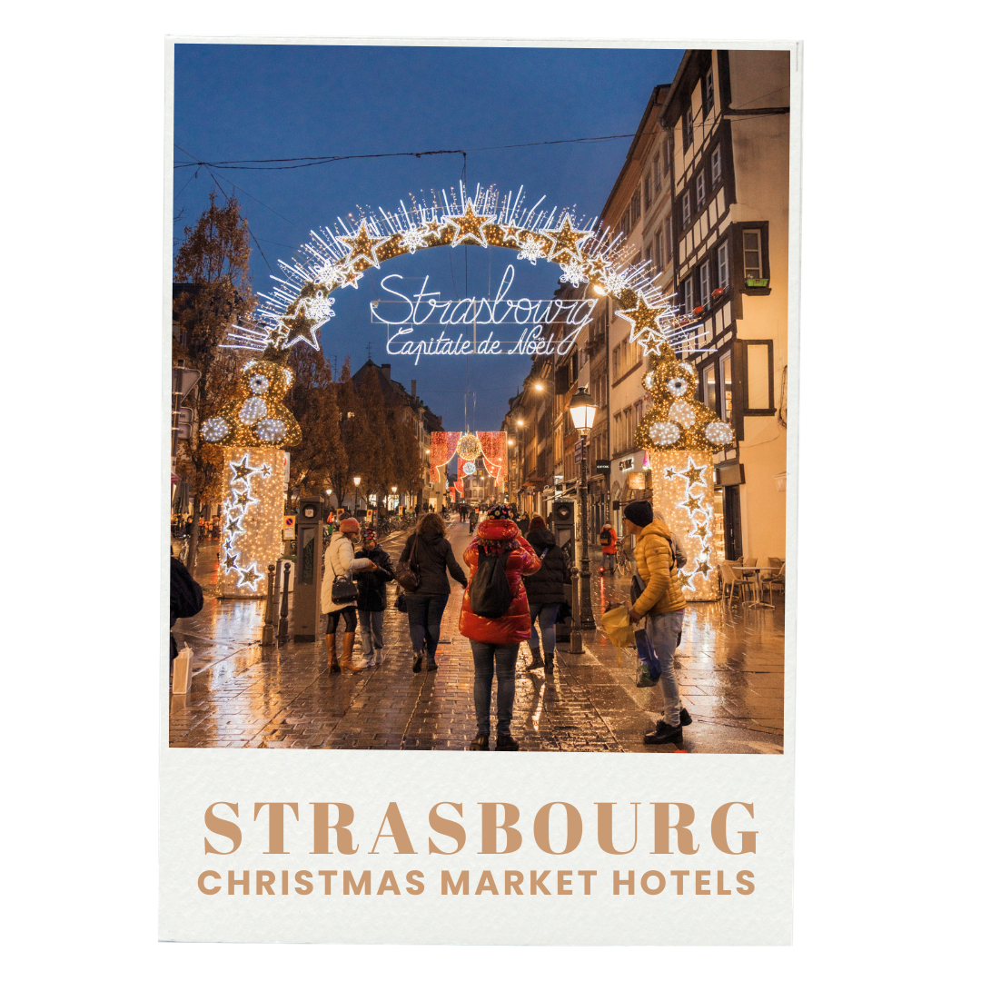 Nighttime scene in Strasbourg with a lit holiday archway that reads 'Strasbourg Capitale de Noël', decorated with stars and teddy bear figures, with people walking on a wet cobblestone street under decorated christmas lights.