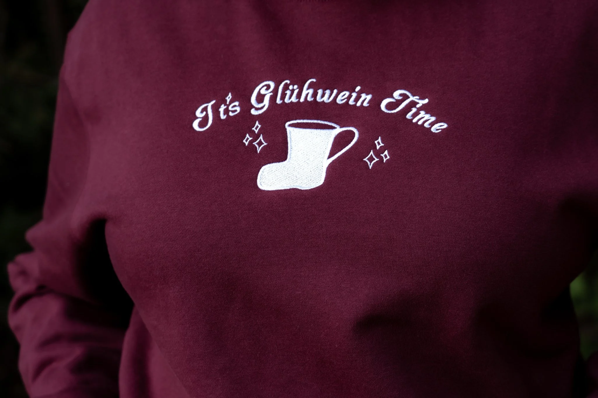 A close-up of a maroon sweatshirt with a white design of a sock and the phrase "It's Glühwein Time" surrounded by small stars.