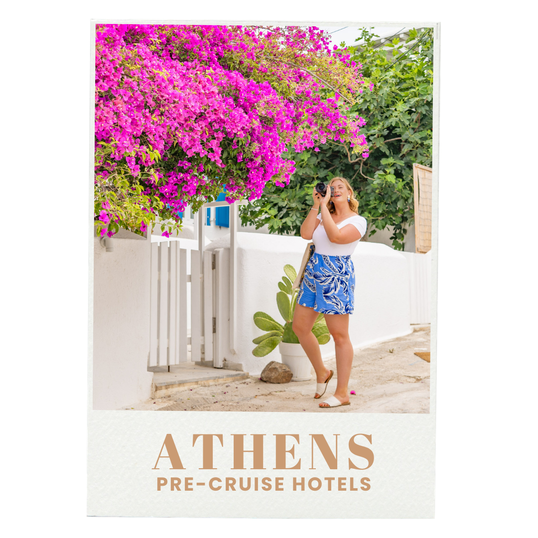 A woman with blonde hair wearing a white top and blue patterned shorts takes a photo with a camera in front of a white wall and vibrant pink bougainvillea flowers in Athens, Greece.