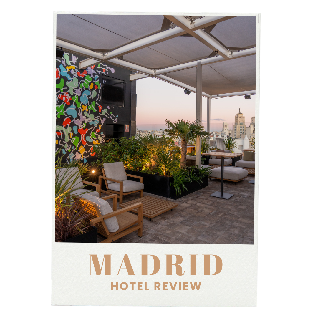 A rooftop terrace with lounge chairs, plants, and city skyline view at sunset, with a cityscape including tall buildings in Madrid, Spain.