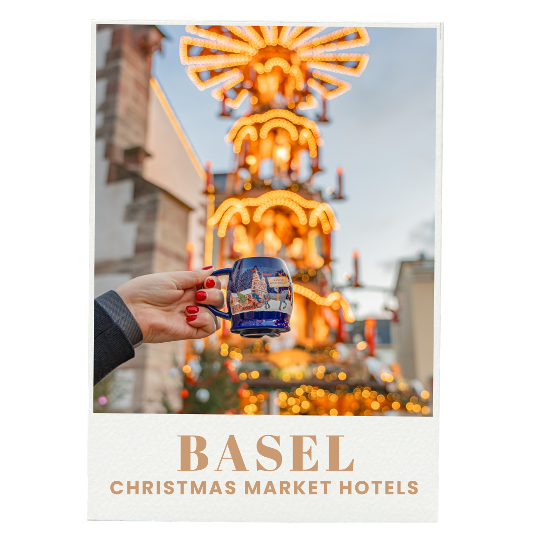 A person's hand holding a blue mug with a logo, in front of a brightly lit carnival ride at dusk, with the words "Basel Christmas Market Hotels" at the bottom of the image.