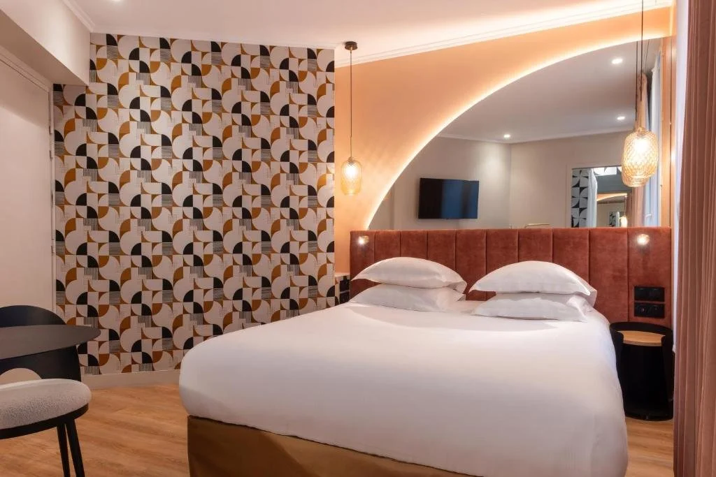 Hotel room with a bed, patterned accent wall, wall-mounted TV, pendant lights, and a mirror.