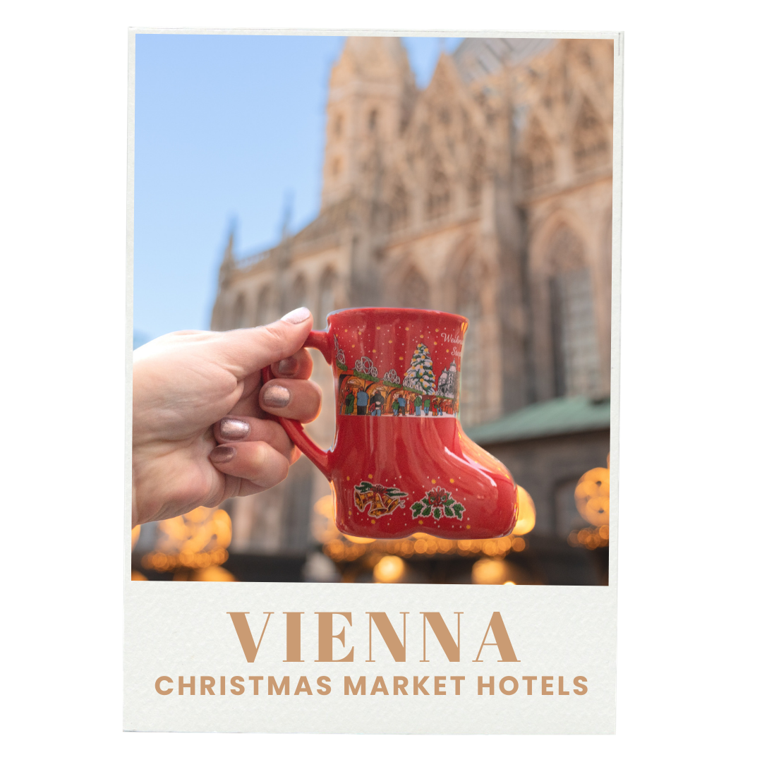 A hand holding a red Christmas mug with holiday designs in front of a blurred background of a historic building and Christmas lights in Vienna.