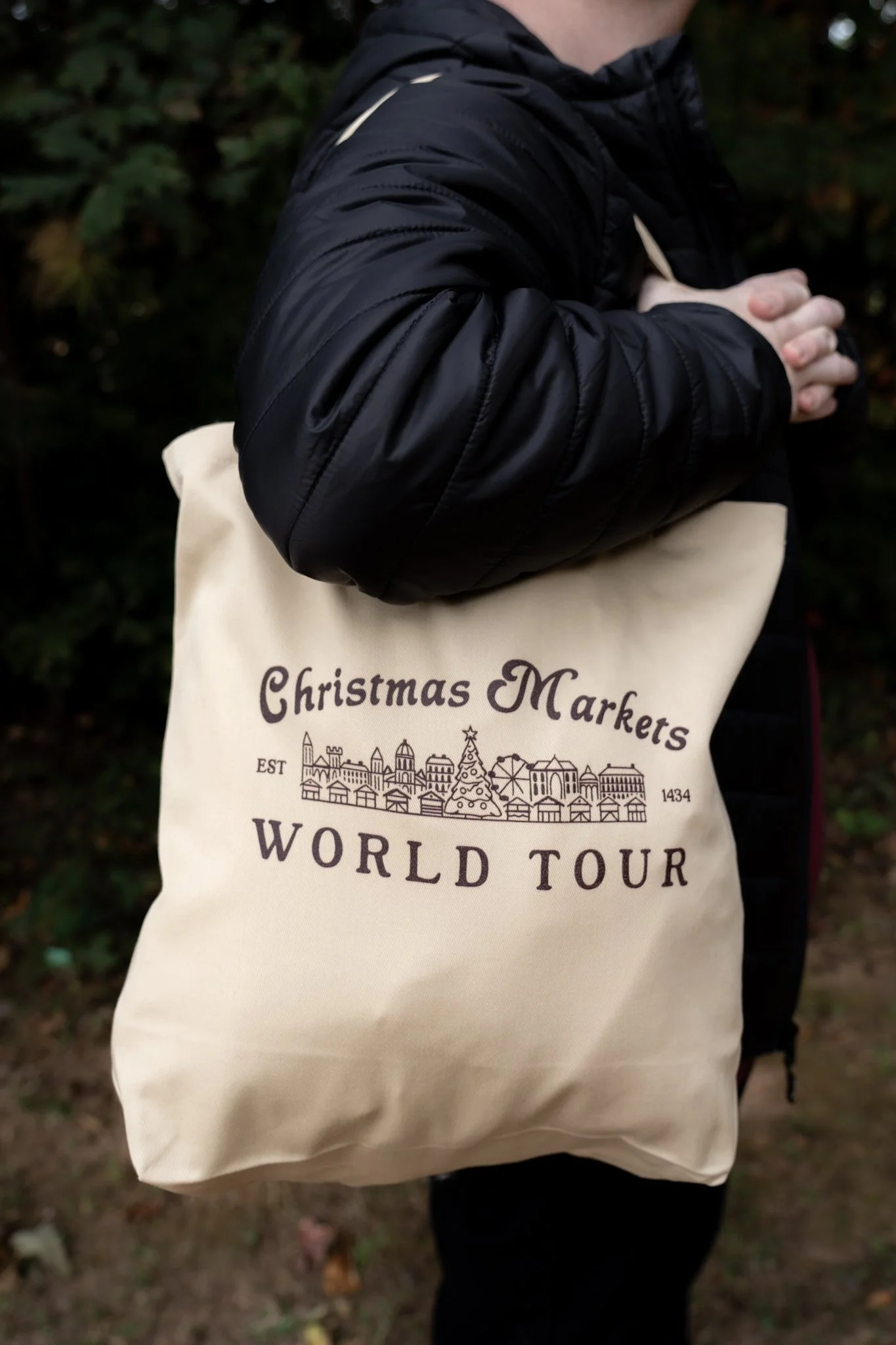 A person holding a beige bag with the text 'Christmas Markets World Tour' and cityscape illustration printed on it.