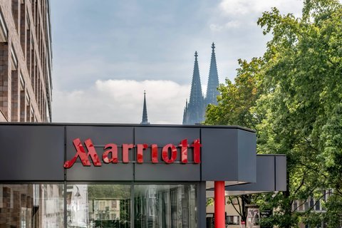 Exterior of a Marriott hotel with the city skyline and trees in the background.