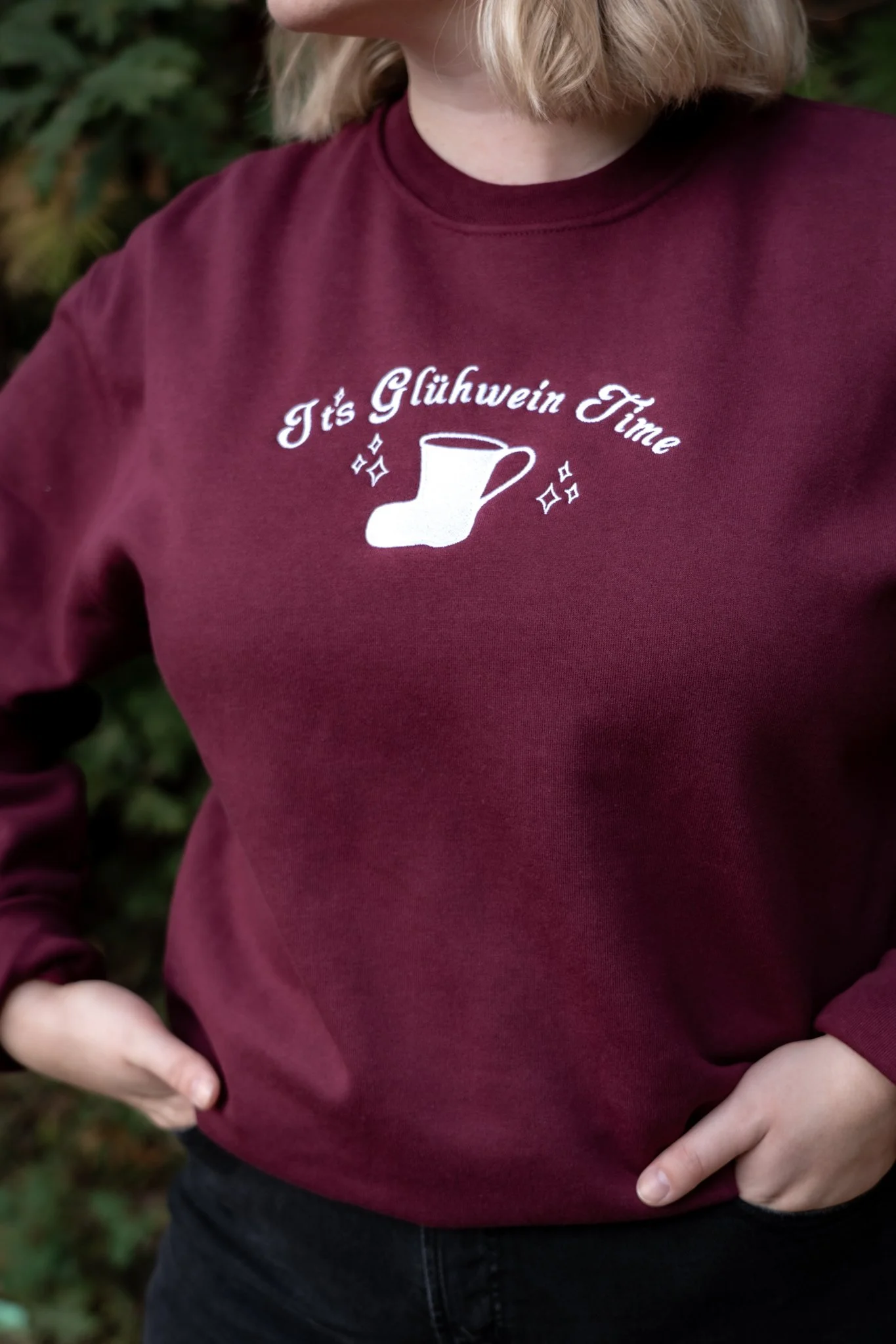 Maroon sweatshirt with white text reading "It's Glühwein Time" and a graphic of a mug with sparkling effects.