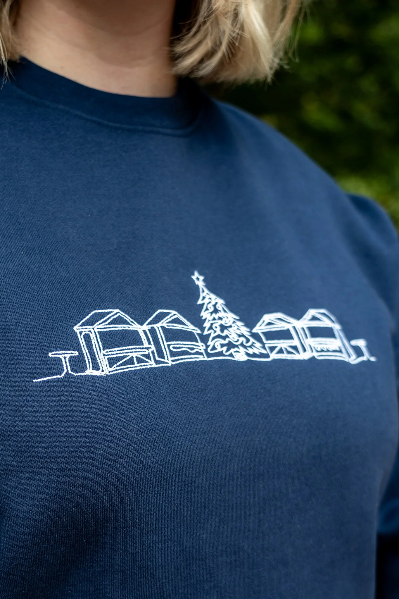 Close-up of a navy blue T-shirt with a white embroidered design of houses and a Christmas tree.