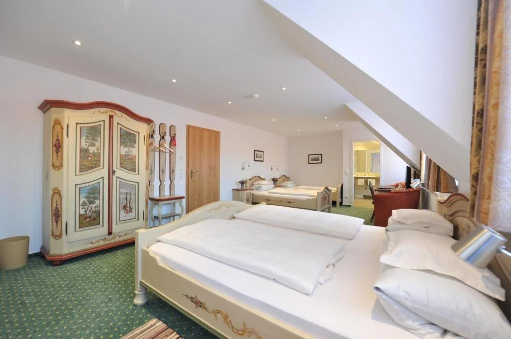 Spacious hotel room with multiple beds, vintage furniture, and a small bathroom visible in the background.