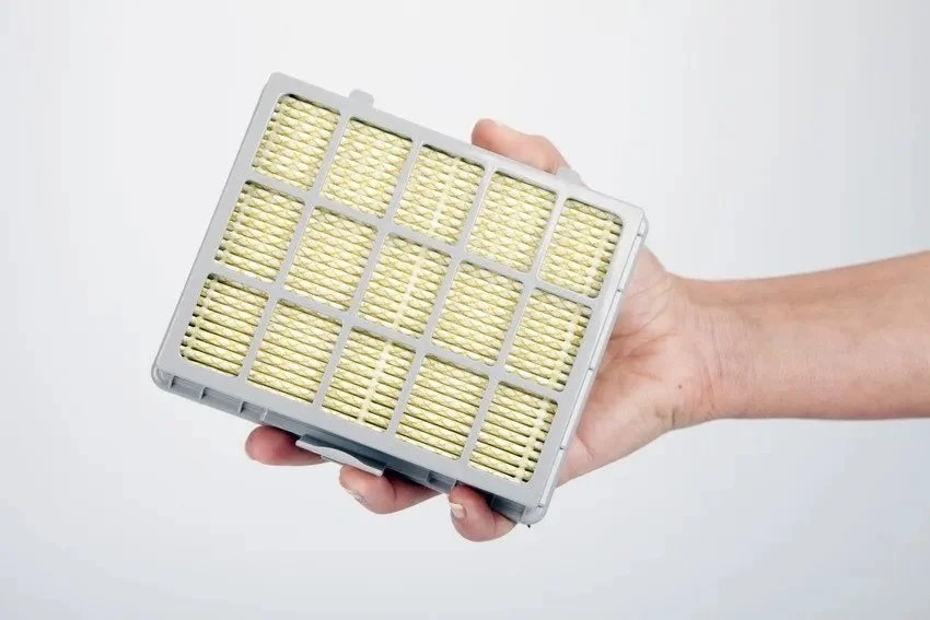 Person holding a square air filter with yellow pleated material and gray frame