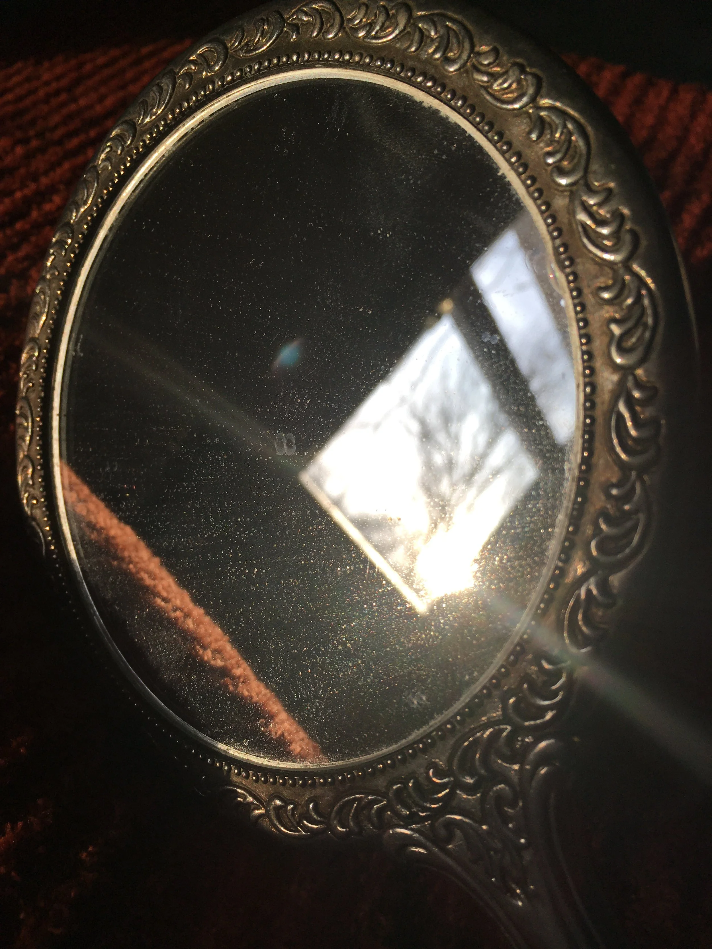 A vintage handheld mirror reflects a ray of sunlight in an otherwise darkened room.