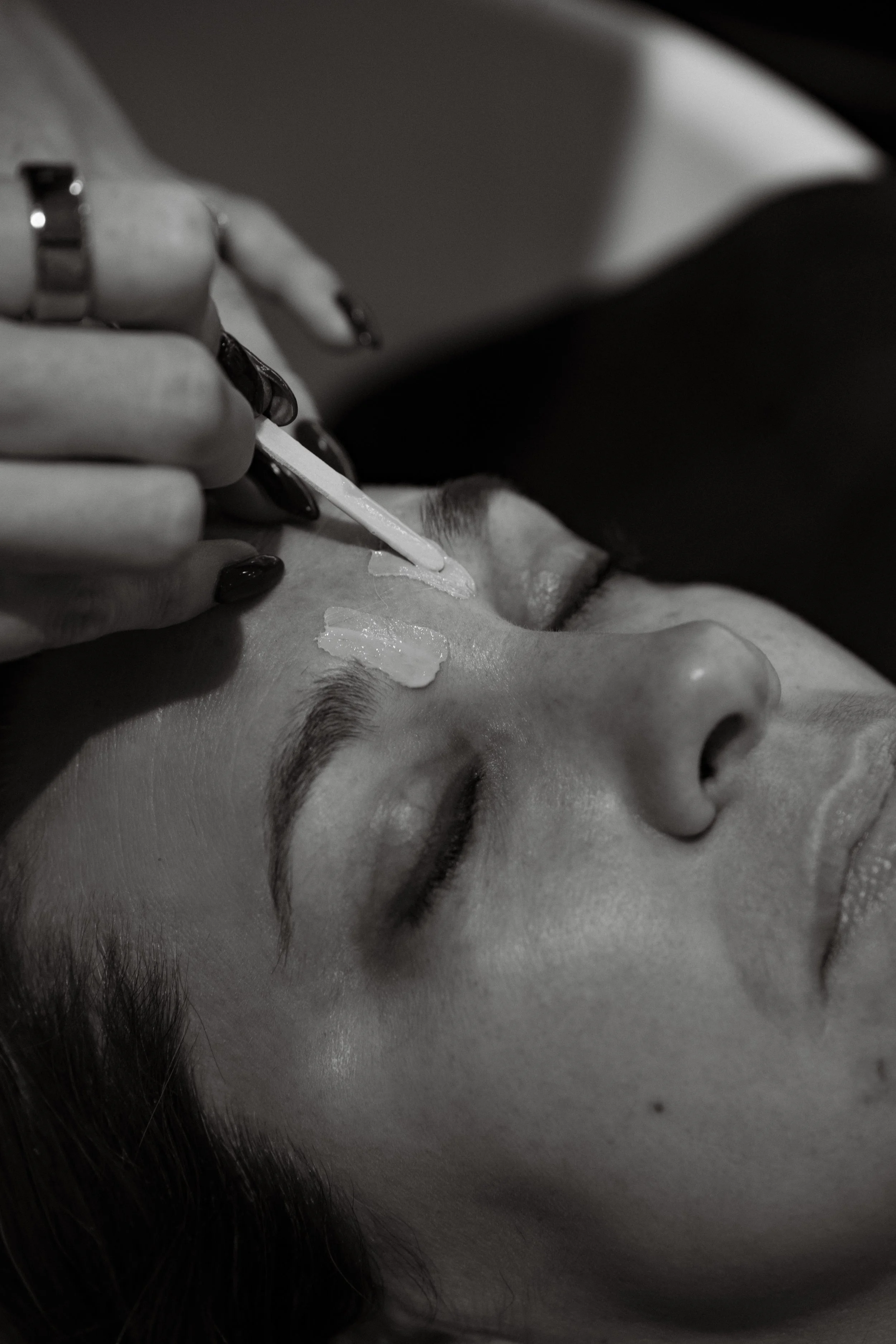 Esthetician applying wax to a client's eyebrows with the clients eyes closed.