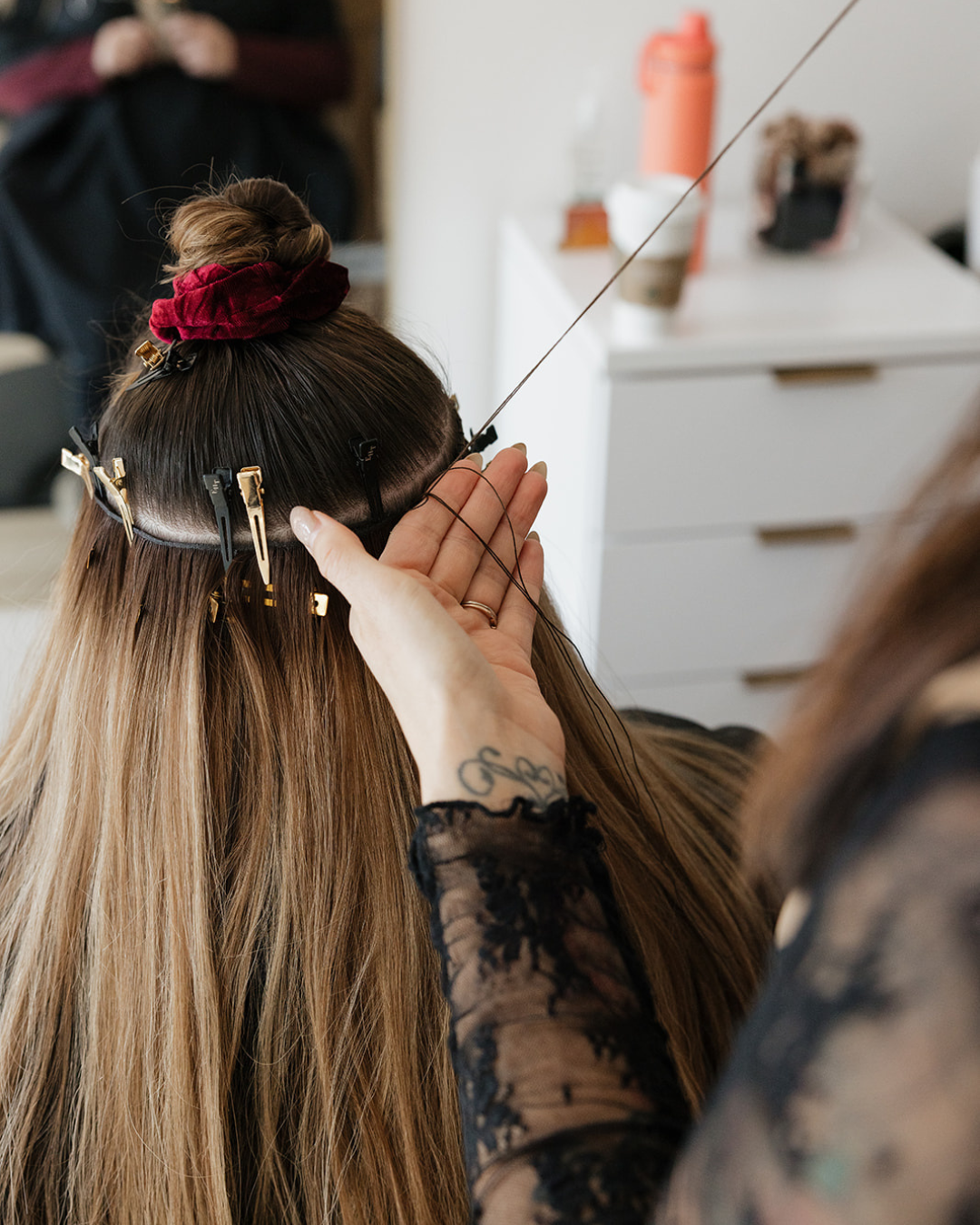 A hairstylist adjusting hair clips in a client's long, blonde hair while applying hair extensions.