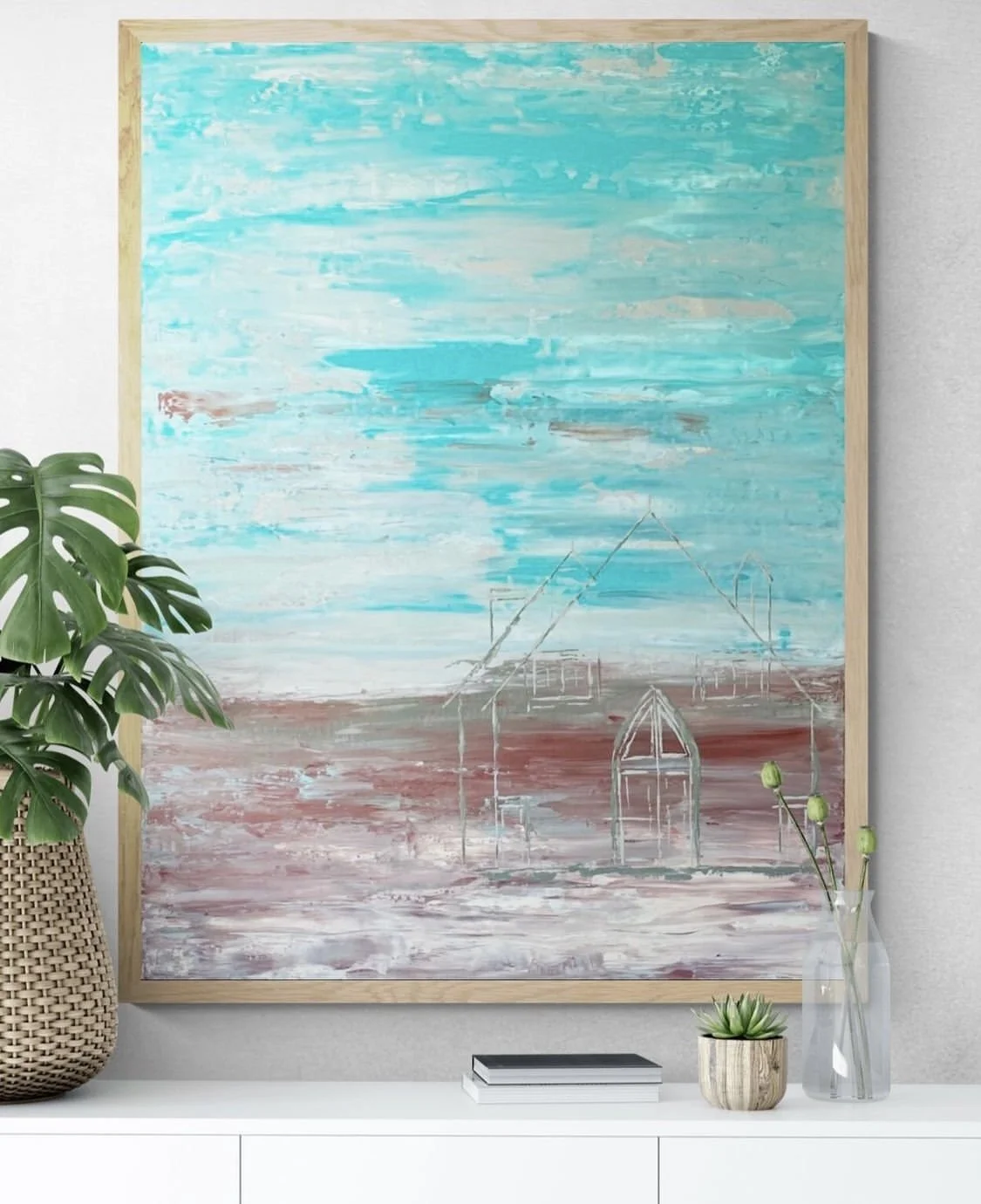 Abstract painting of a beach scene with blue sky and water, white structures resembling houses or boats, and a sandy foreground, hanging on a wall.