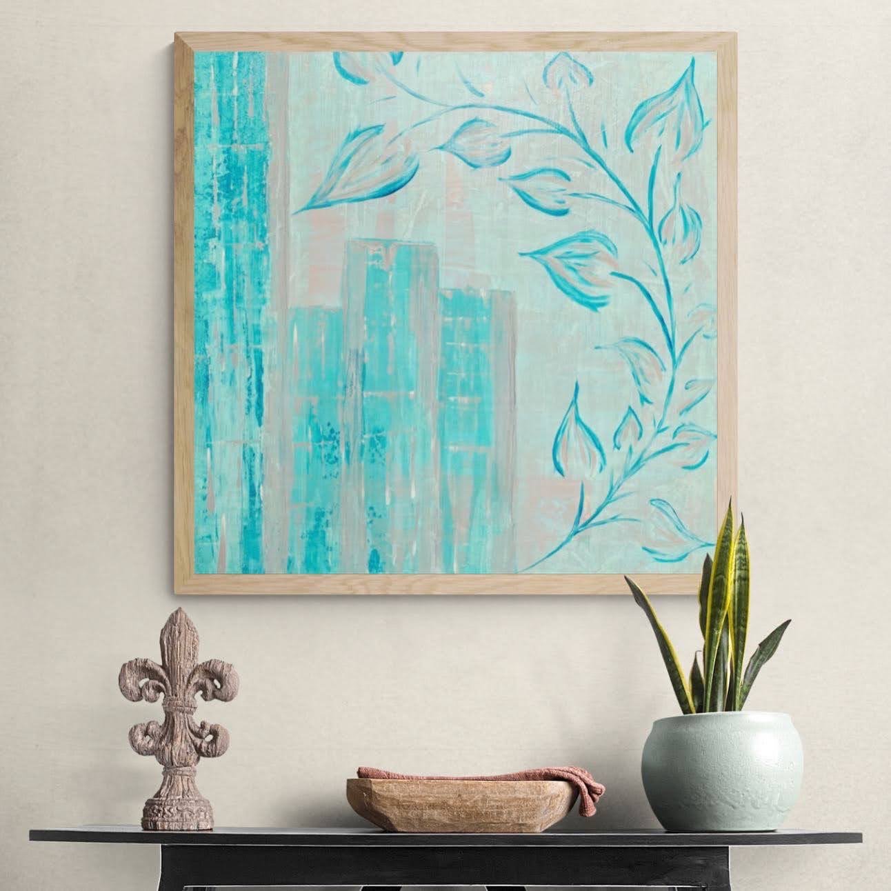 A wall art painting with abstract blue city skyline and floral design in a wooden frame, above a black table holding a decorative stone sculpture, a wooden bowl with a pink cloth, and a green snake plant in a white pot.