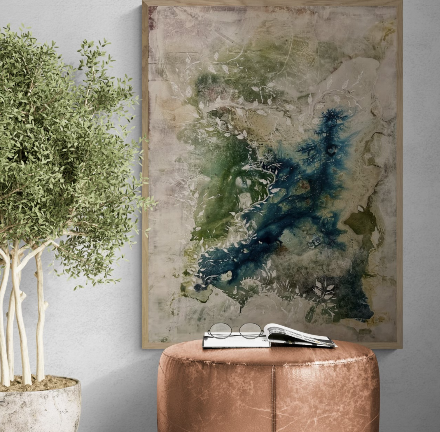 A modern interior scene with a green potted plant on the left, an abstract watercolor painting with green and blue accents in a wooden frame on the wall, and a pink velvet ottoman with glasses, a notebook, and a magazine on top.