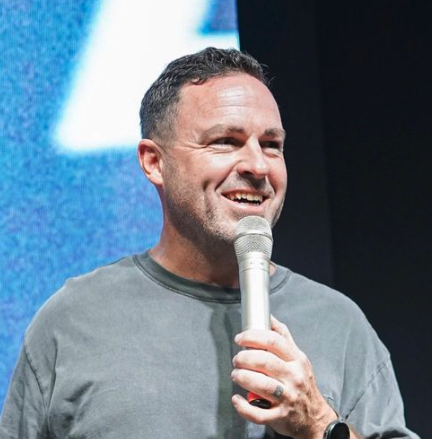 Man smiling and speaking into a microphone on stage.