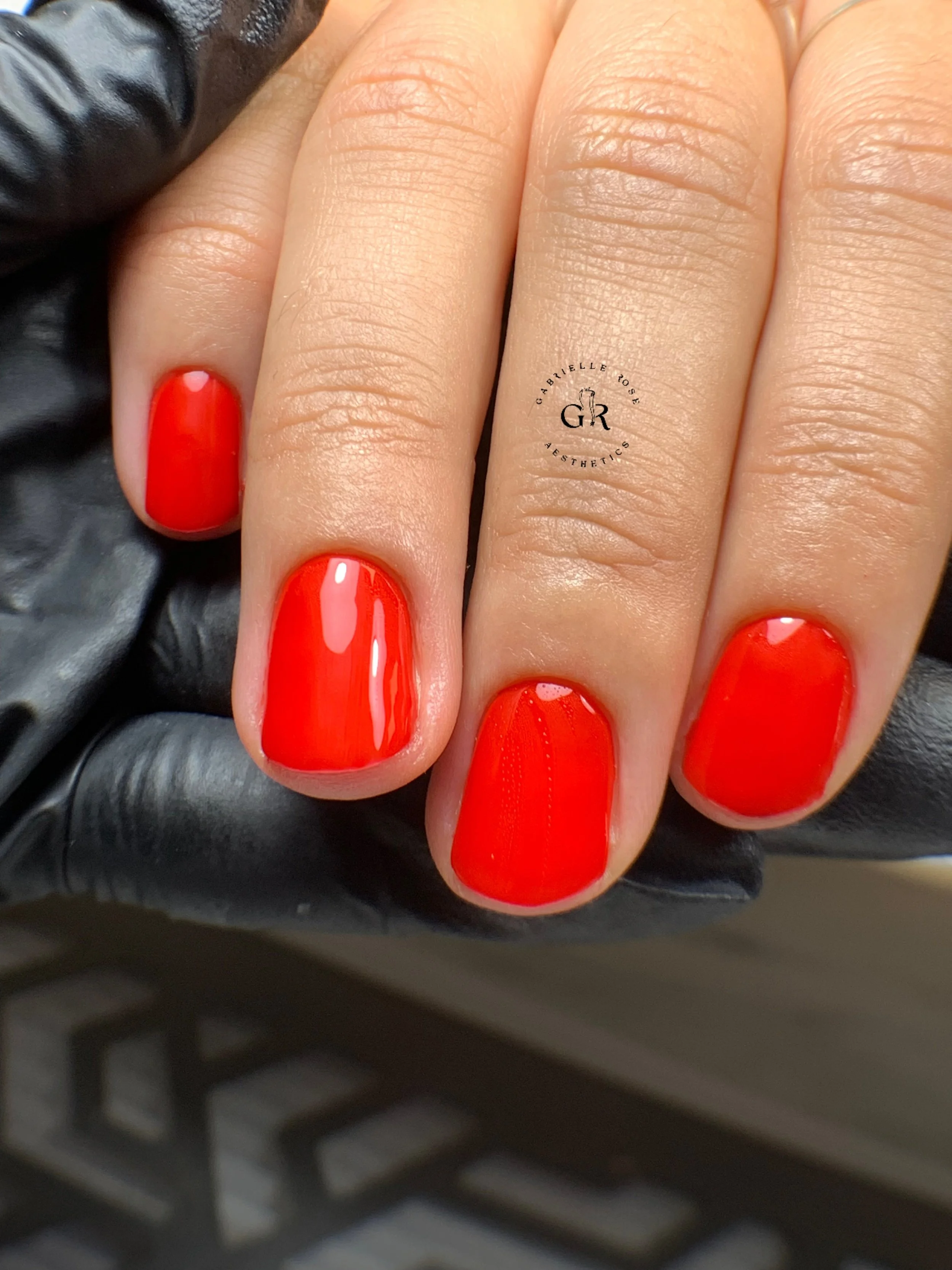 Doigts avec ongles peints en rouge brillant, posés sur une main portant un gant noir en cuir.