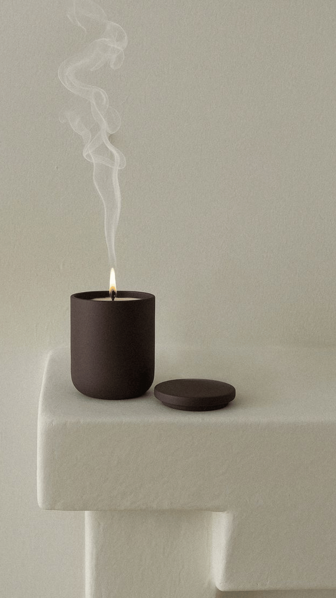 Une bougie noire allumée sur une petite table blanche avec de la fumée qui s'élève de la flamme. La table a une surface en forme de cube.