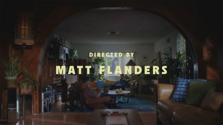 Living room scene with two people sitting on chairs, coffee table, and plants, with yellow text overlay reading 'Directed by Matt Flanders'.