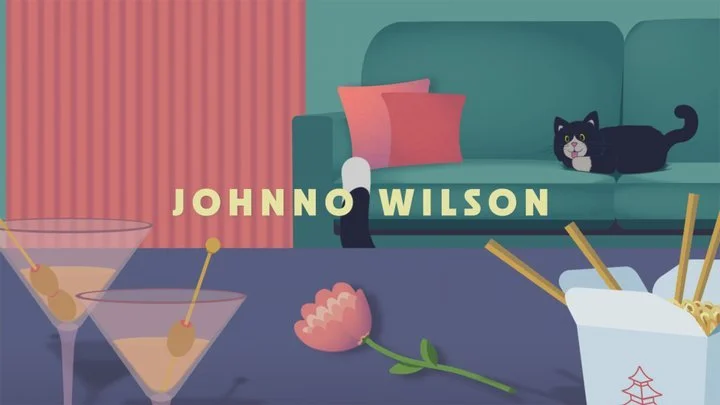 A colorful animated scene with the name 'Johnny Wilson' displayed. There are two martini glasses with olives on a table, a pink flower, and a bowl of spaghetti with chopsticks. In the background, a black cat is lying on a teal sofa, and a small white dog stands on the floor facing the sofa. Pink curtains are partially visible behind the sofa.