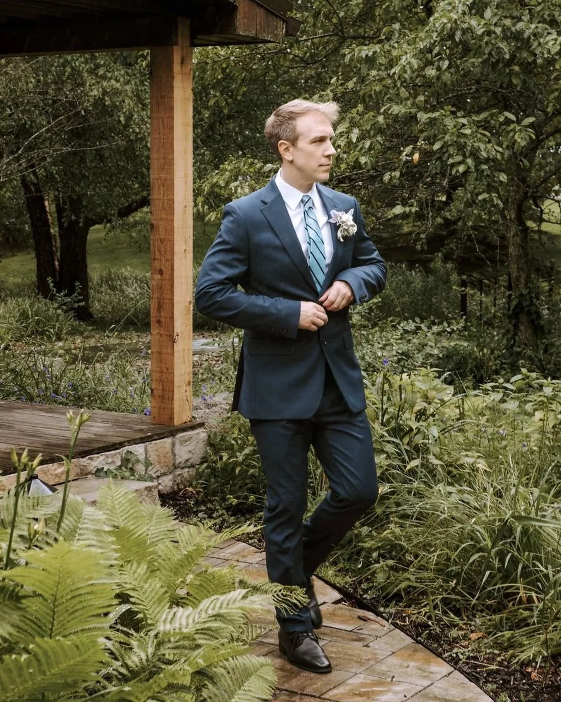 Brett Hammon, Pittsburgh wedding videographer, in a navy suit in a garden