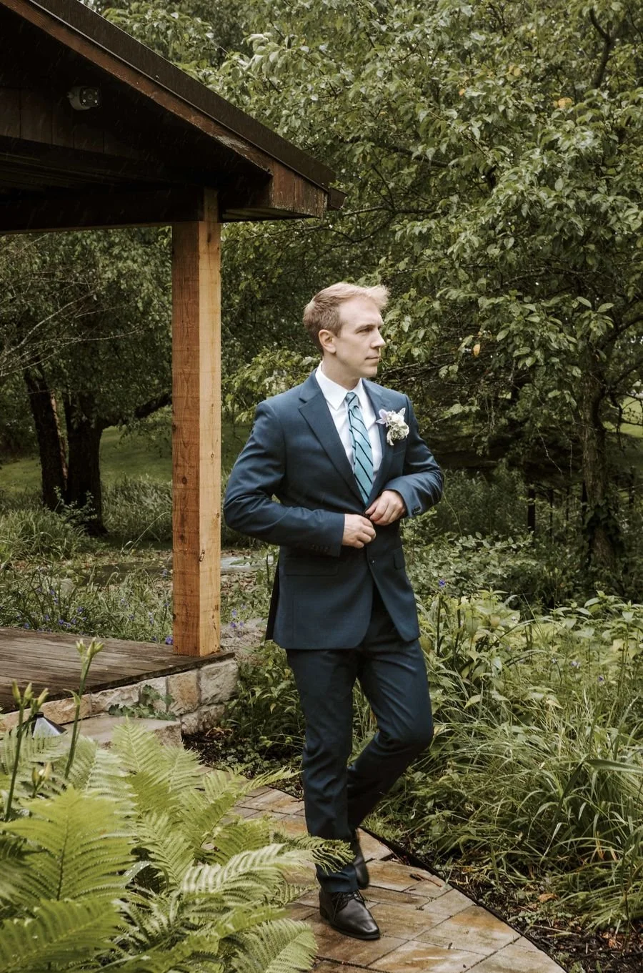 Brett Hammon, South Hills wedding videographer, in a navy suit in a garden