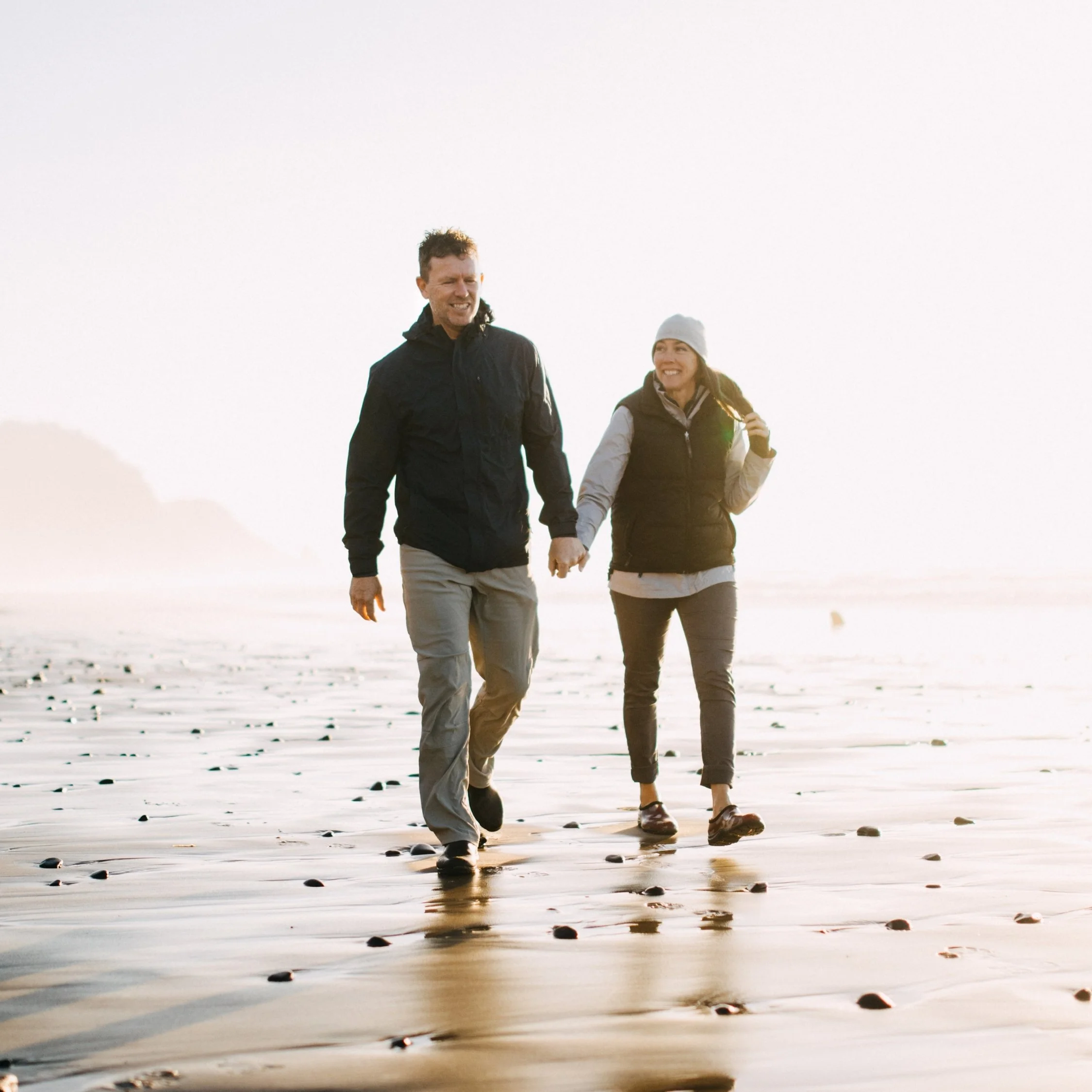 Couple holding hands while walking along the beach at sunset.