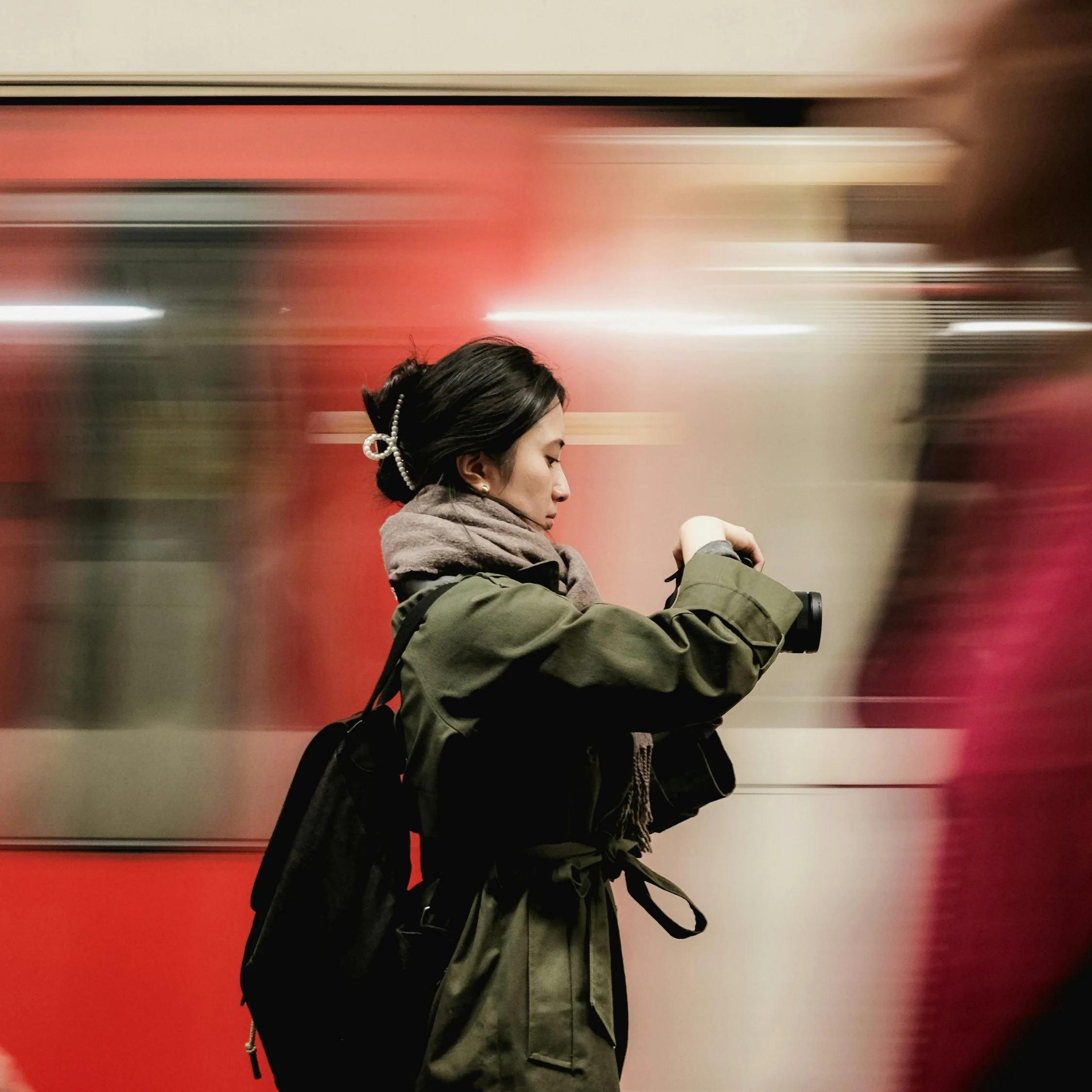 Woman standing in subway station checking her camera, capturing a mindful moment in a busy city.