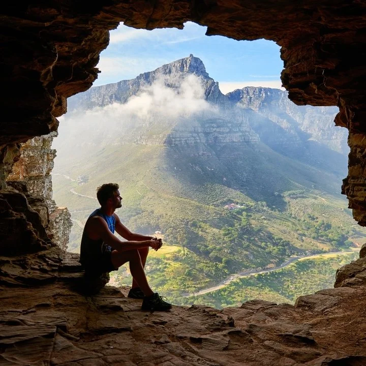 Man sitting inside cave opening overlooking mountain valley.