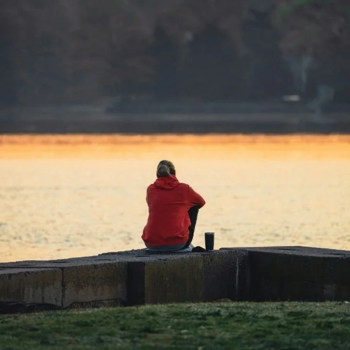 Person sitting alone by the water reflecting before therapy.