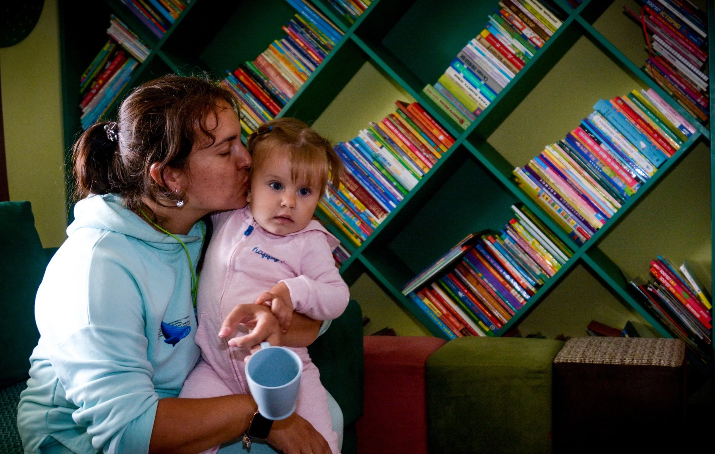A mother kisses her toddler while sitting in the shelter's library