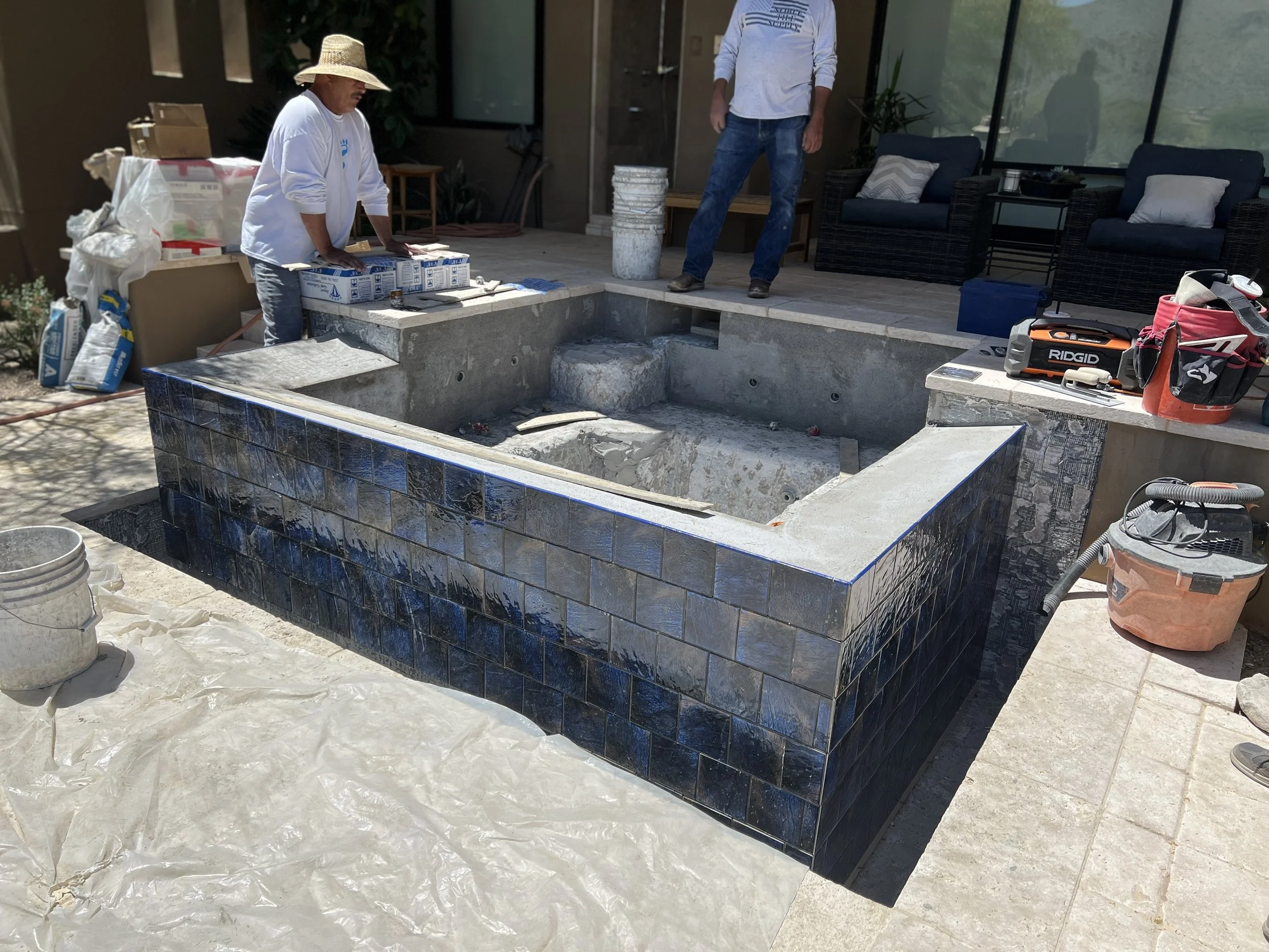 Progress photo of a Phoenix spa renovation showing new $6" \times 6"$ blue tiles installed on the exterior walls and negative edge basin.